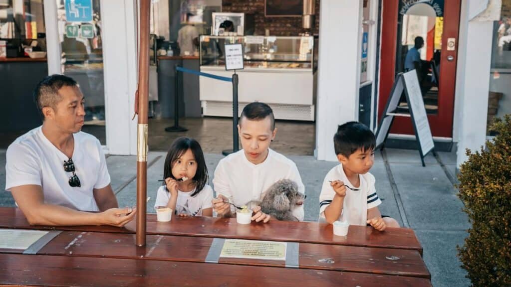 A family of four shares ice cream together at an outdoor seating near an ice cream shop.