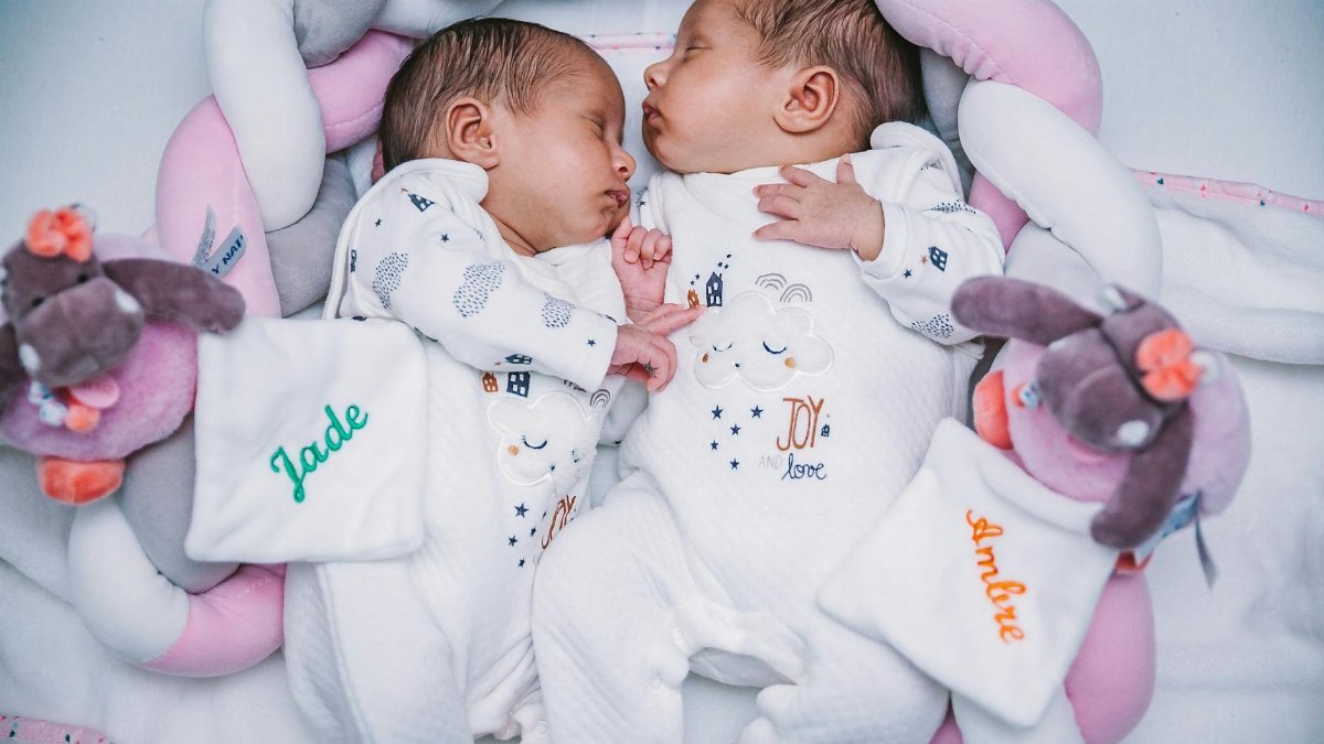 Cute twin babies peacefully sleeping with plush toys, wearing matching pajamas indoors.