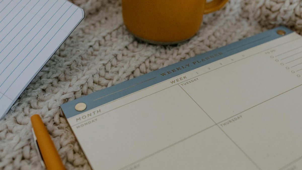 A cozy workspace featuring a weekly planner, pen, and coffee mug on knitted fabric. Perfect for planning.