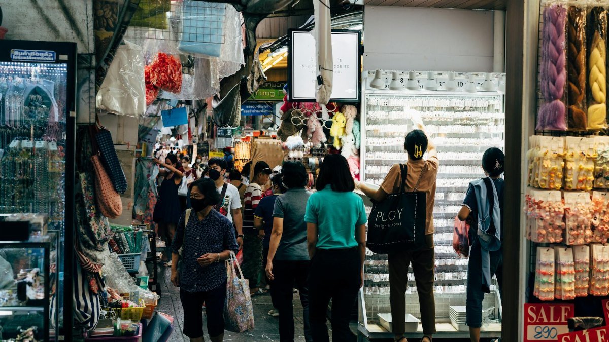 A busy marketplace filled with people shopping among colorful stalls and various goods.