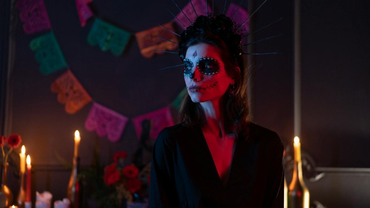 Woman dressed for Day of the Dead with face paint and headdress in a festive setting.