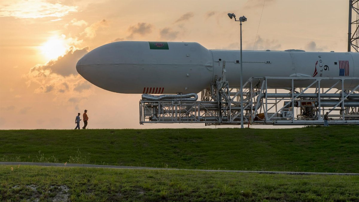 A space shuttle on a launchpad with people walking nearby at sunset.