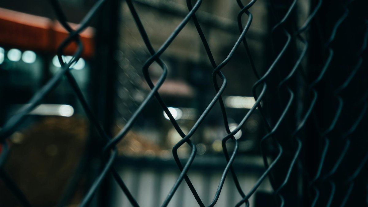 Close-up of a chain link fence with bokeh lights in the background, creating a moody atmosphere.
