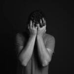 A grayscale portrait of a man covering his face, depicting emotion and mental health themes.