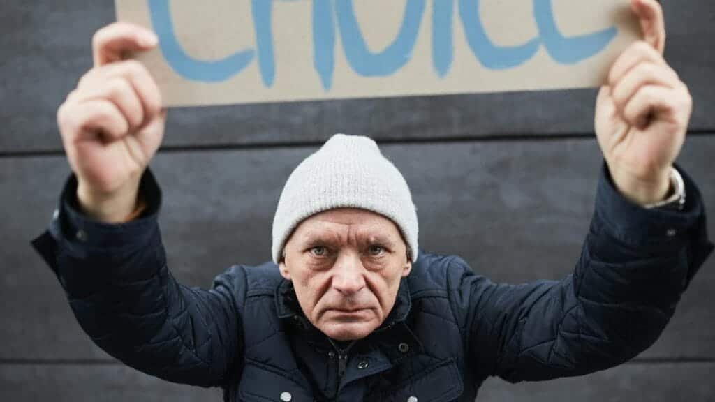 Determined man in beanie holds protest sign with 'Choice' outdoors.