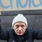 Determined man in beanie holds protest sign with 'Choice' outdoors.