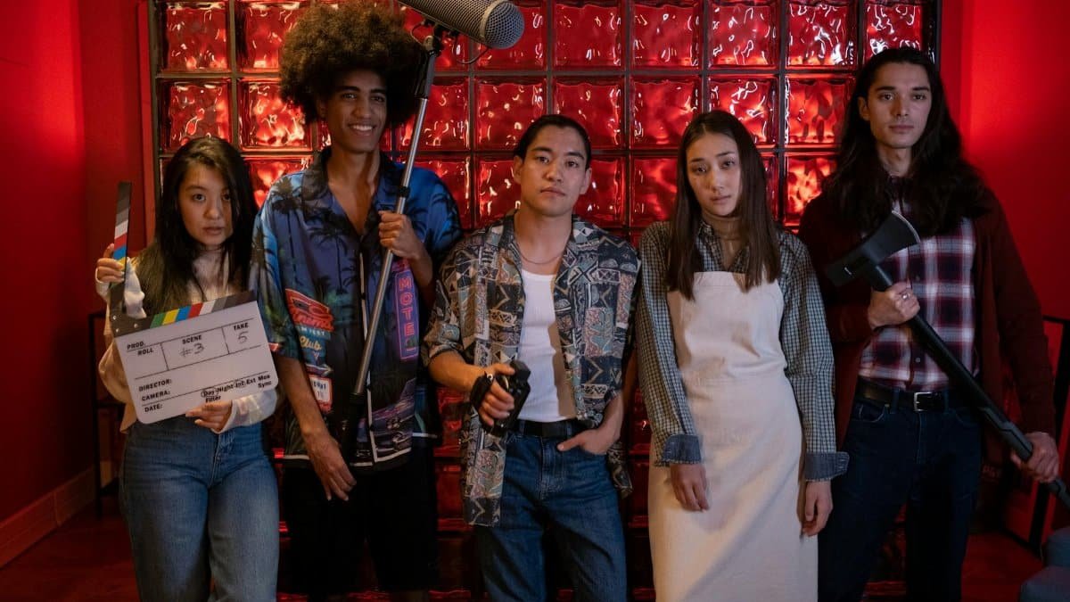 A diverse group of five people standing with film equipment indoors. Creative scene with vibrant red background.