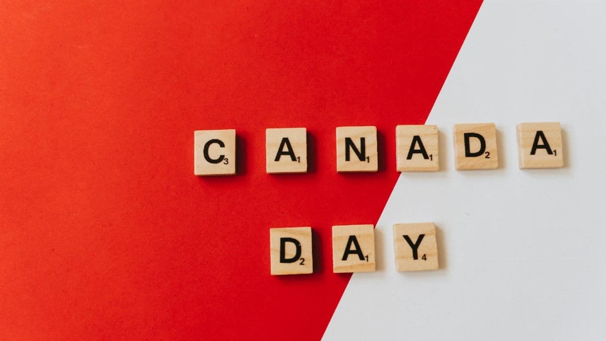 Wooden Scrabble tiles on a red and white background spell out Canada Day, symbolizing celebration and national pride.