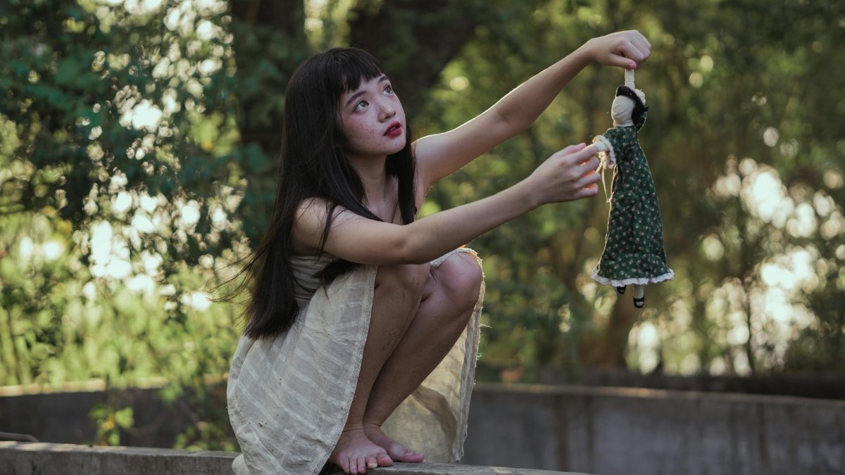A young woman crouching and playing with a vintage doll in a serene outdoor setting.