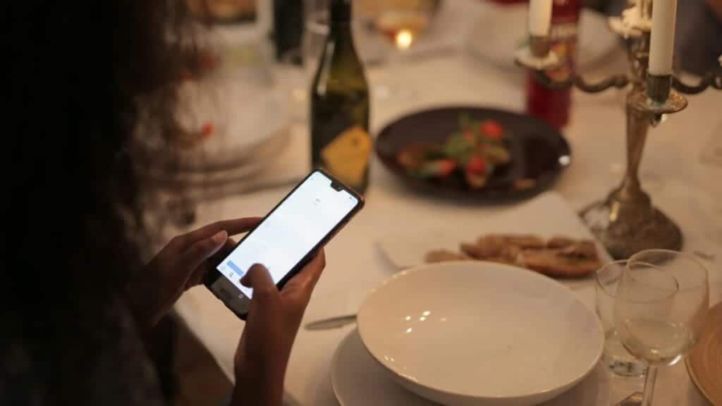 A cozy dinner setting with a woman using a smartphone at a candlelit table.