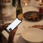 A cozy dinner setting with a woman using a smartphone at a candlelit table.