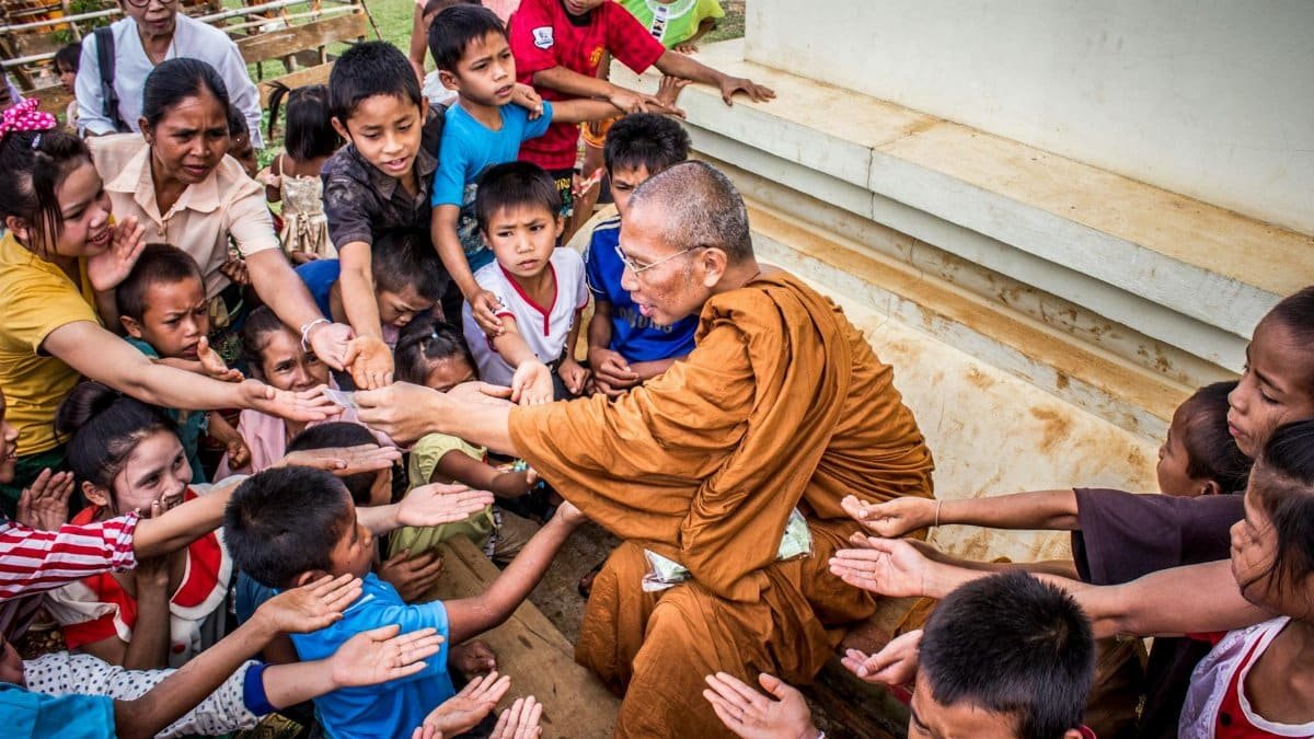 A Buddhist monk sharing gifts with children, capturing a moment of compassion and cultural tradition.