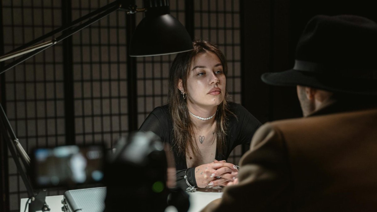 A dramatic scene of two adults in a dimly lit interrogation room, captured from a unique angle.
