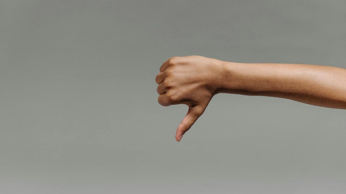 Close-up of a person's hand giving a thumbs down gesture against a gray background.