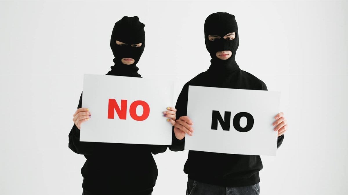 Two masked individuals holding "No" signs against a white background, concept of refusal or anonymity.