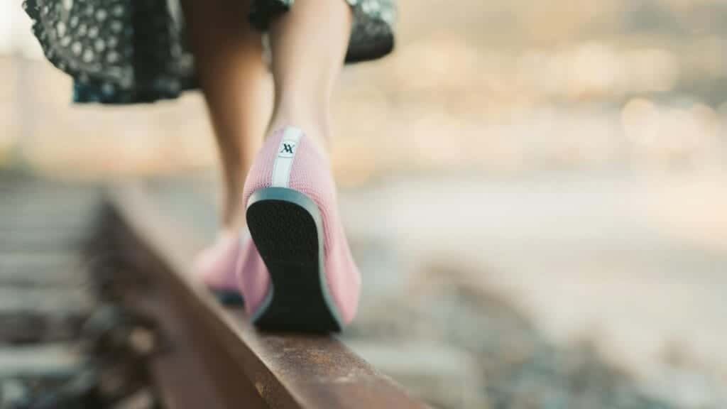 Fashionable woman in pink shoes walking on a railway track during summer, showcasing leisure and style.
