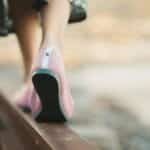 Fashionable woman in pink shoes walking on a railway track during summer, showcasing leisure and style.