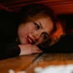 A distressed woman lying under a wooden structure, expressing fear and anxiety.