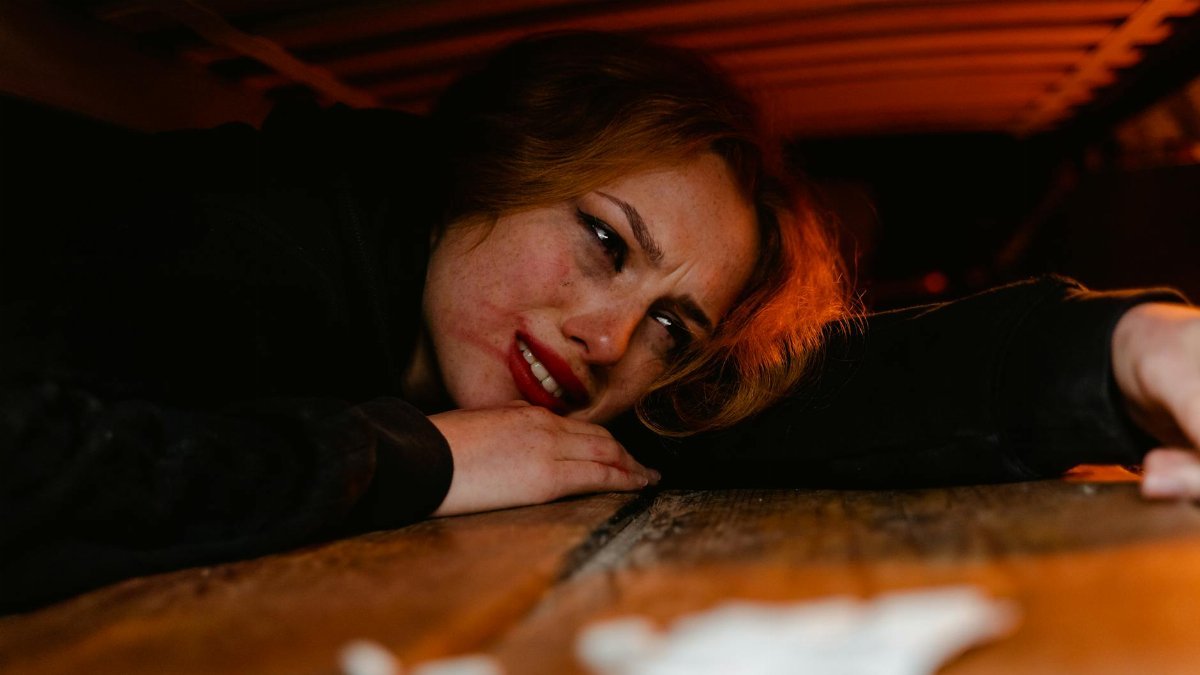 A distressed woman lying under a wooden structure, expressing fear and anxiety.