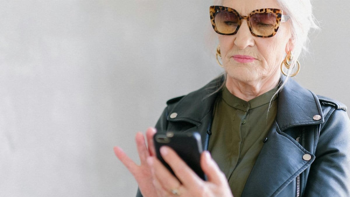 Senior woman in stylish outfit using a smartphone indoors, embodying elegance and tech-savvy living.