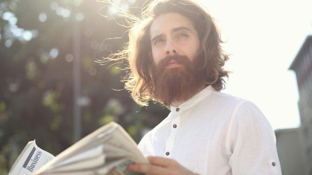 Young bearded man enjoying a sunny day while reading a newspaper outdoors.