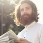 Young bearded man enjoying a sunny day while reading a newspaper outdoors.