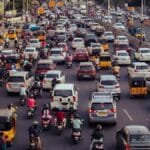 A crowded city street filled with cars, motorcycles, and buses during daytime rush hour.