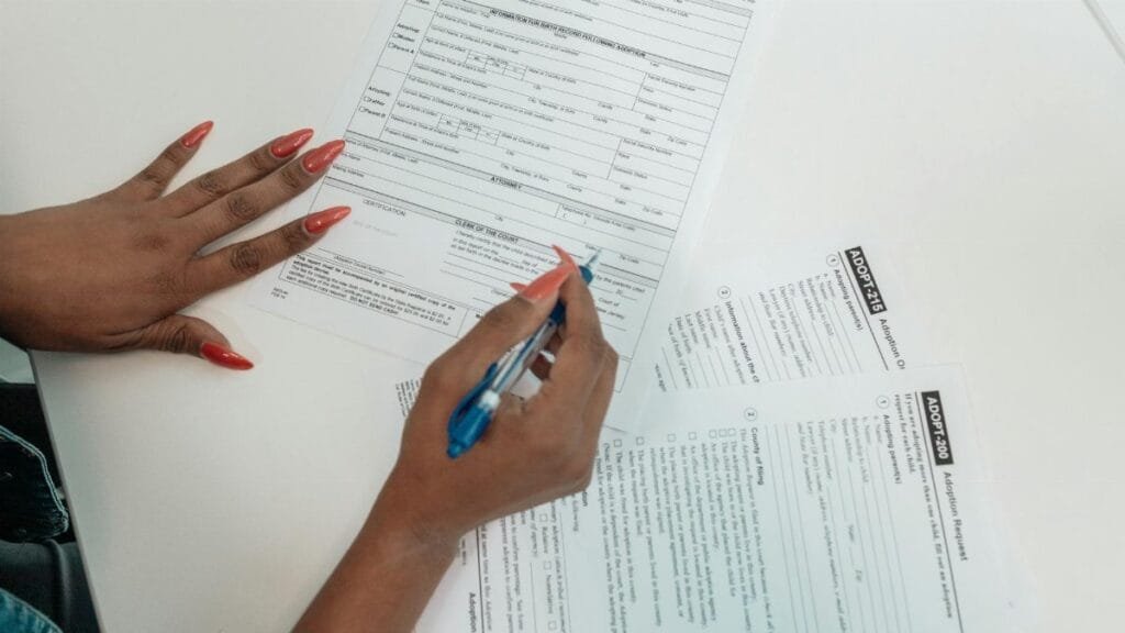 A woman with red nails fills out adoption application forms on a desk.