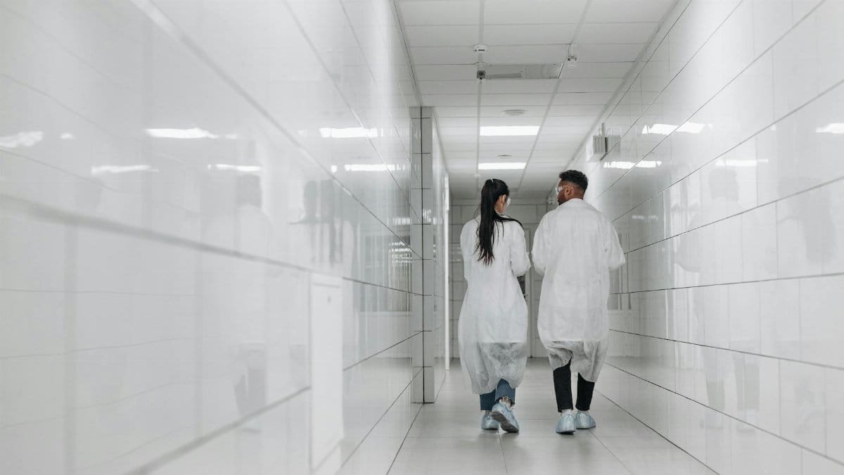 Two scientists in lab coats walk down a bright, tiled hallway, showcasing modern research environment.