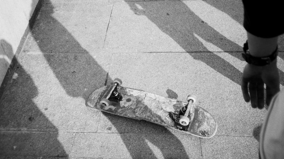 A skateboard lies upside down on a city pavement with surrounding shadows, evoking urban life.