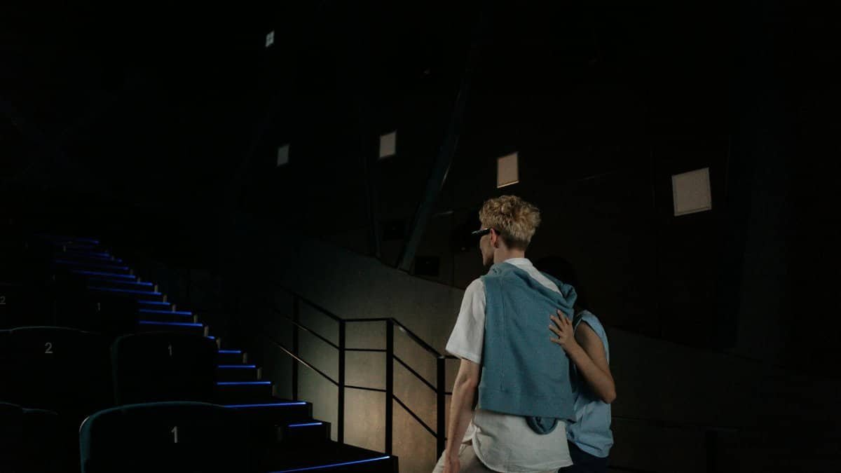 A man guided by an assistant walking upstairs in a dimly lit movie theater.