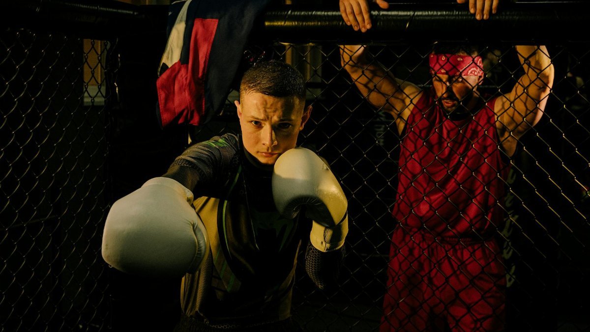 Boxer in white gloves sparring with trainer in a cage fighting ring, martial arts focus.
