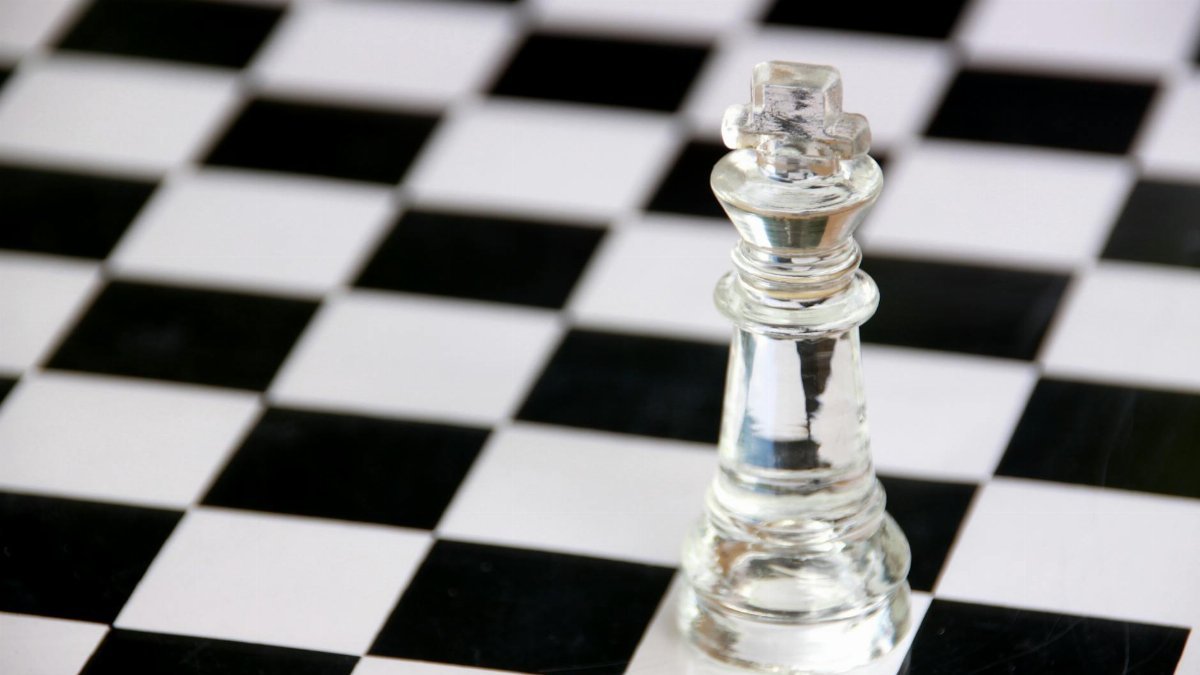 A glass chess king piece on a classic black and white chessboard symbolizes strategy and victory.