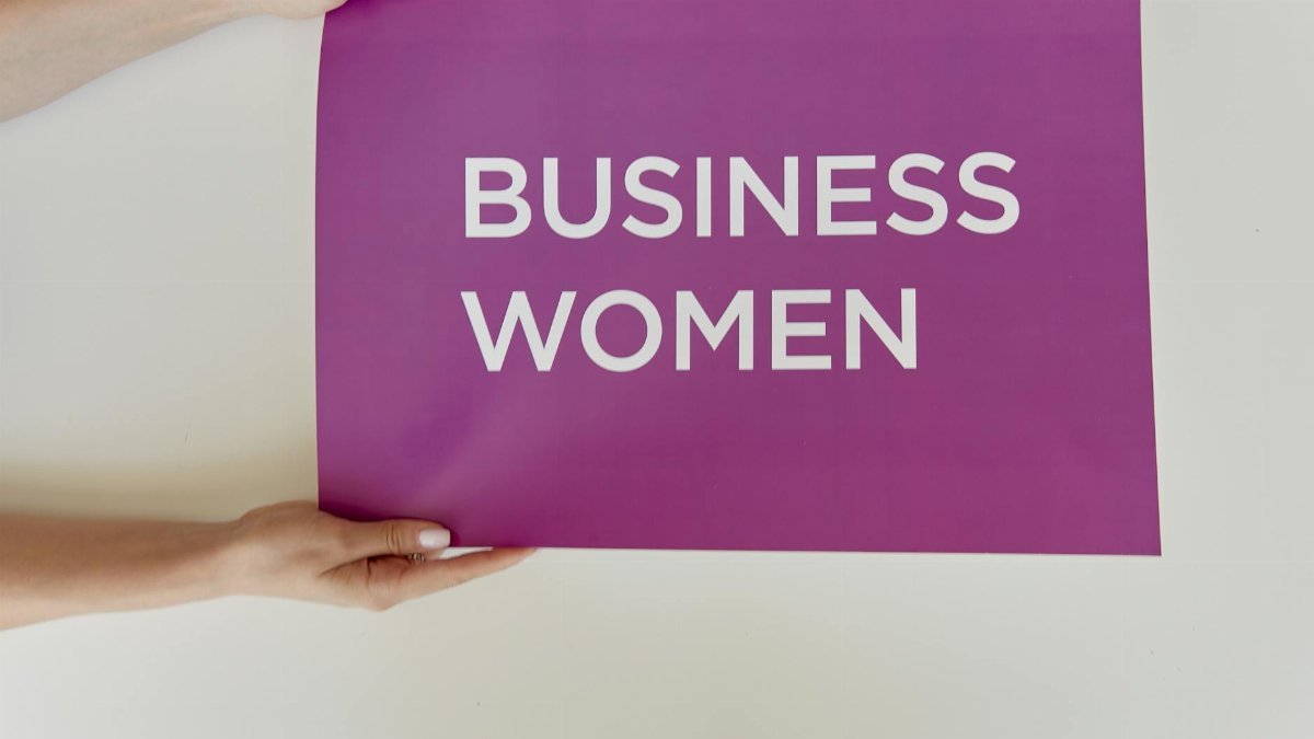 Hands holding a purple sign with 'Business Women' for empowerment.