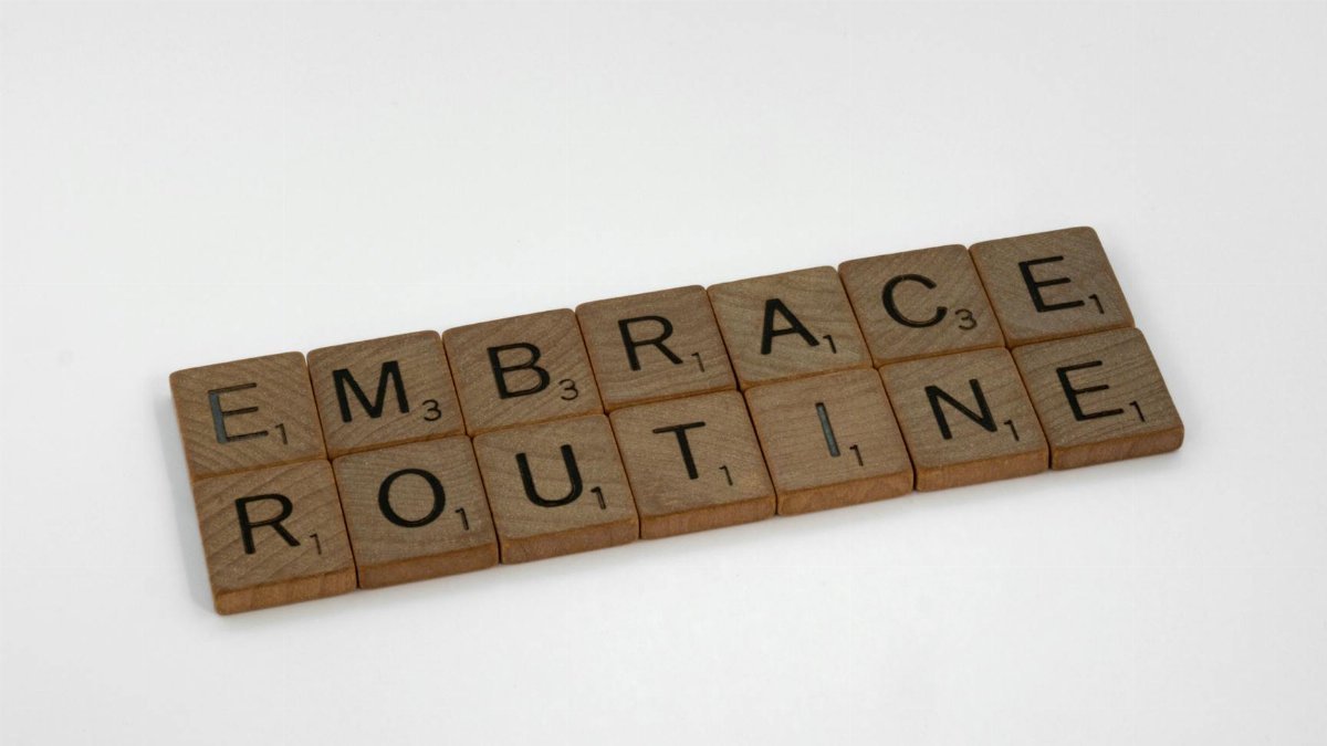 Wooden Scrabble tiles spelling 'Embrace Routine' on a clean white background. Perfect for lifestyle and typography concepts.