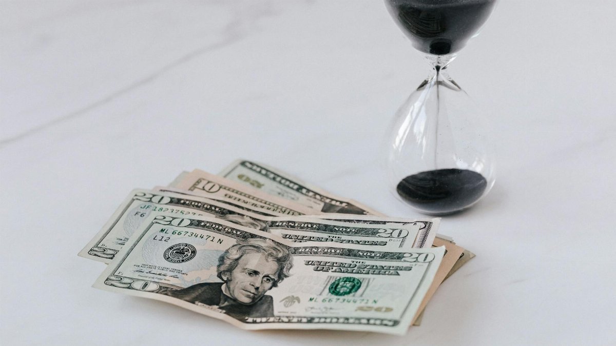Close-up of US dollar bills with an hourglass, symbolizing time and money.