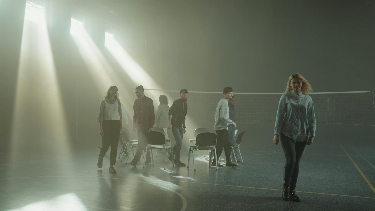 Group of people walking inside a smoky room with dramatic sunrays streaming through windows.