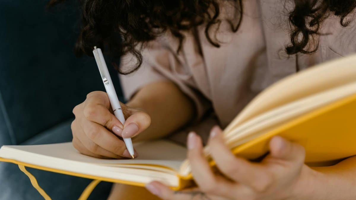 Person writing in a yellow notebook indoors, focusing on ideas.