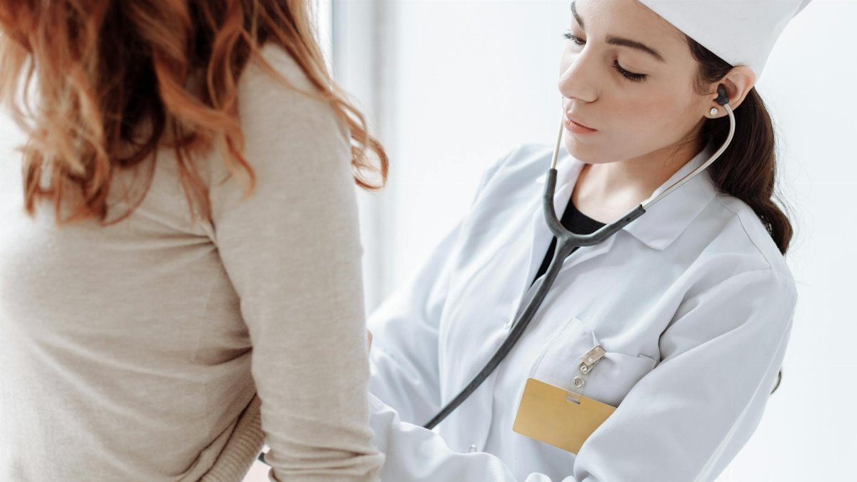 A female doctor in a white coat using a stethoscope during a patient examination.