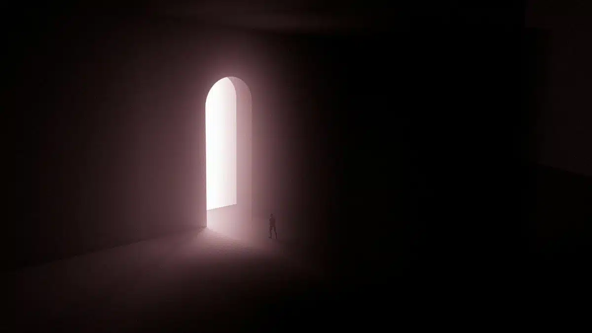 A surreal scene with a lone silhouette in front of an illuminated arched gateway.