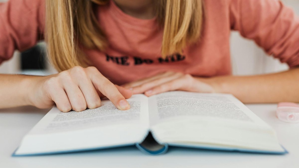 Close-up of a young person reading a book indoors, focusing on hand and text.