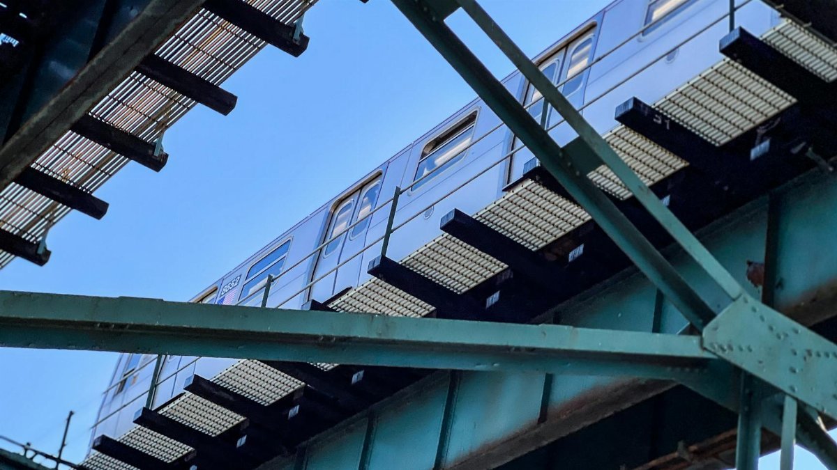A subway train travels on an elevated track in New York City under a clear blue sky.