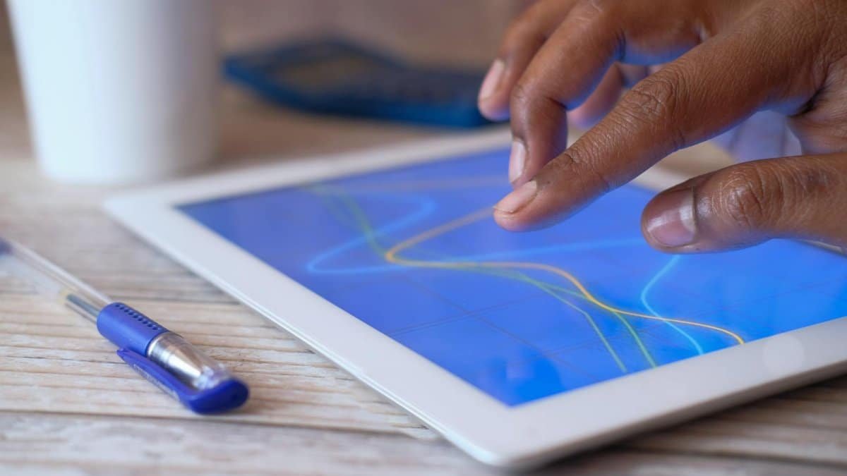 A hand interacting with a digital tablet on a wooden table, showcasing modern technology.