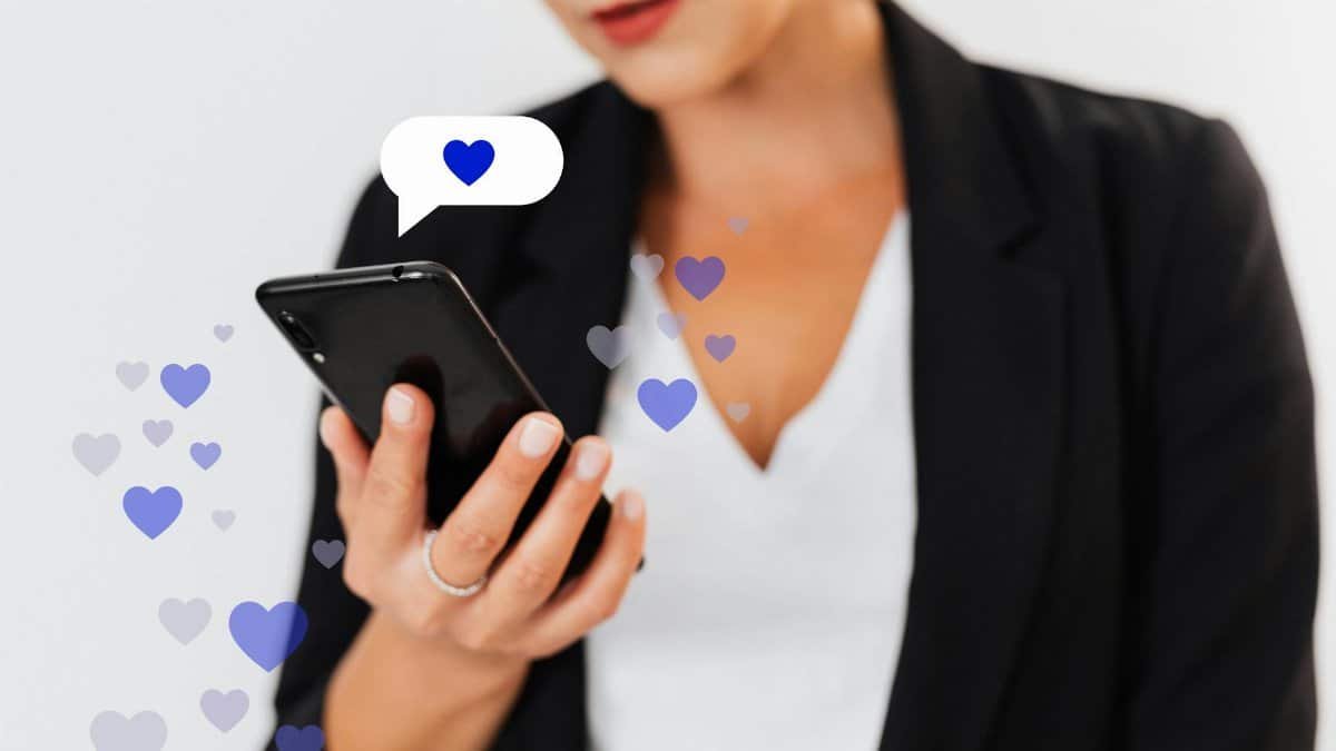 Close-up of a woman holding a smartphone with floating heart icons, illustrating digital engagement.