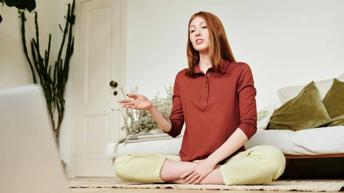 A woman in a lotus position attends an online class from her living room, showcasing modern technology and wellness.