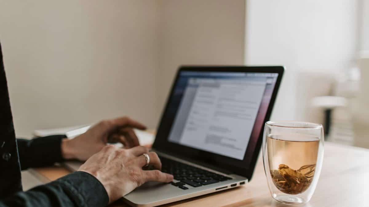 Adult working on laptop with a cup of tea, showcasing remote work lifestyle.