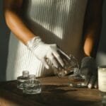 Unrecognizable crop African American female pouring essential oil in glass bottle while making liquid incense at table