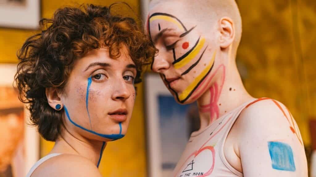 Close-up portrait of two women with vibrant face paint, expressing creativity and intimacy.