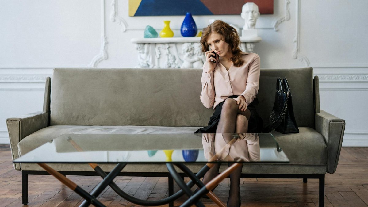 A woman sits thoughtfully on a sofa, engaged in a phone call in a stylish living room.