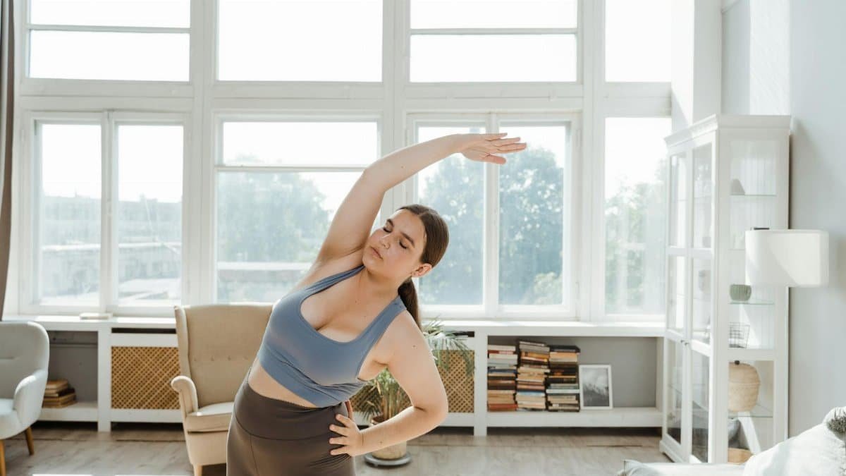 A plus size woman stretches energetically in a sunlit room, promoting body positivity and wellness.